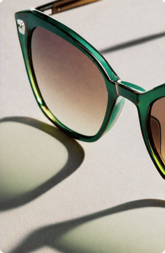 A closeup of a green and tan designer sunglasses resting on a neutral surface illuminated by natural light.