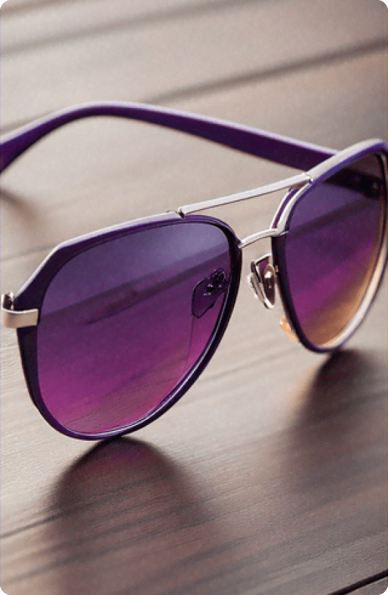 A pair of sleek purple sunglasses with a modern design resting on a smooth wooden table.